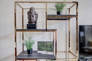 Una estantería met álica de tres niveles con una estatua de Buda en el nivel superior, dos macetas con plantas en el nivel central y el inferior, y una foto enmarcada con la etiqueta "SAVANNAH" en el nivel inferior.