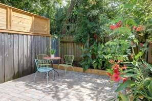 A patio with two metal chairs and a small round table, surrounded by a wooden fence and lush greenery. - Adorable Cottage 2 Blocks From Forsyth Park - B (Savannah)