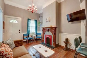 A living room with a fireplace, a television mounted on the wall, and a sofa with patterned cushions. - Adorable Cottage 2 Blocks From Forsyth Park - B (Savannah)