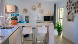 A modern kitchen with a central island, bar stools, a built-in oven, and a flat-screen TV above the island. - APARTMENT SEEVIEW ON THE BEACH PARKING ALL INCLUSIVE TORROX NERJA MALAGA SPAIN (Torrox Costa)