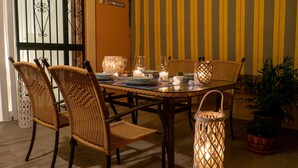 Un coin repas avec des chaises en osier, une table ronde dressée avec des assiettes, des verres et des bougies.
