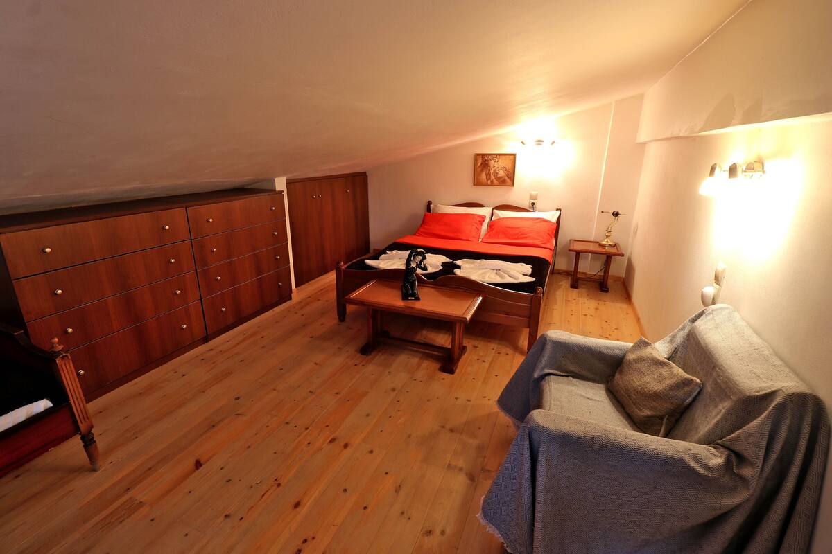 A bedroom with a bed, a wooden dresser, a small table, and a couch.