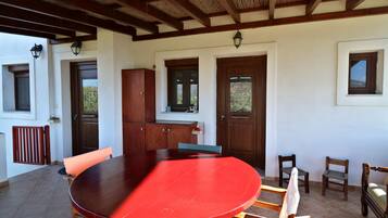 A covered patio area with a red table, wooden chairs, a cabinet, and a door with a window.