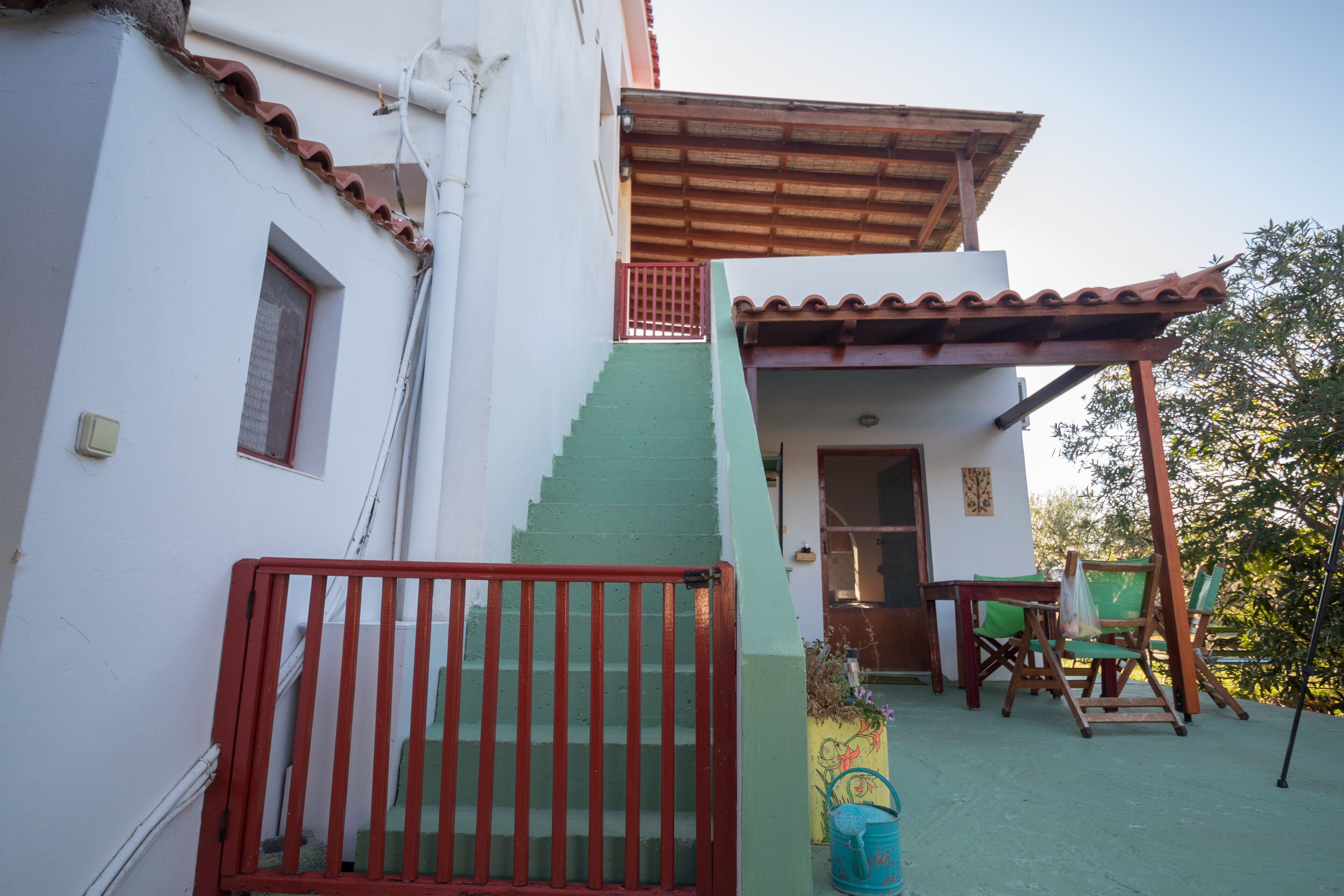 A white building with a green staircase, a red gate, and a wooden pergola.