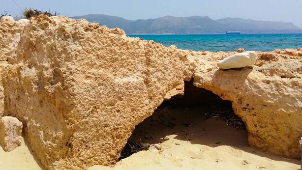 Un paisaje costero rocoso con un mar azul claro y montañas distantes.