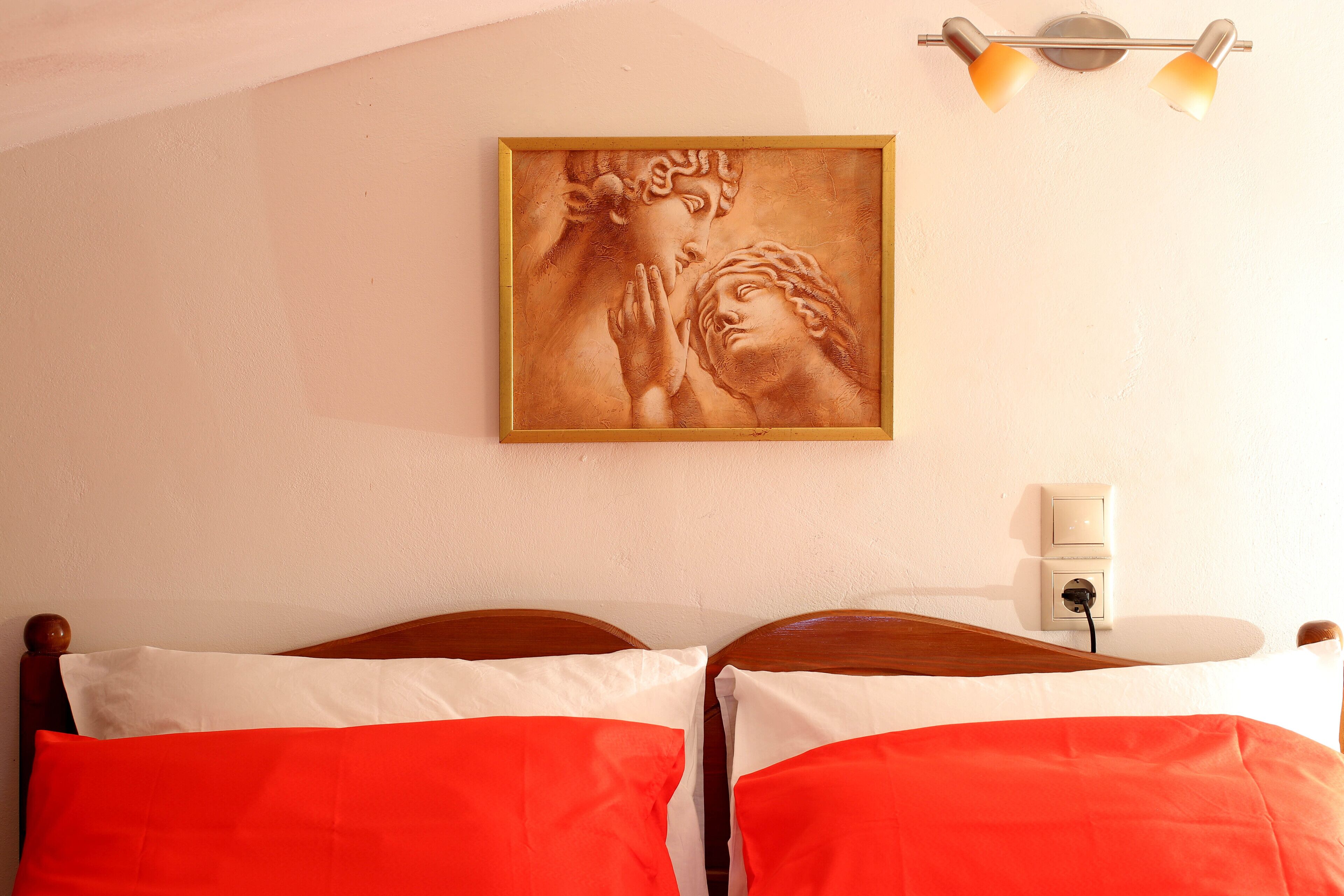 A bedroom with two beds, a wall-mounted light fixture, and a framed artwork.