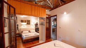 Un dormitorio con techo de madera, una cama con ropa blanca, un armario de madera y un espejo que refleja parte de la habitación.