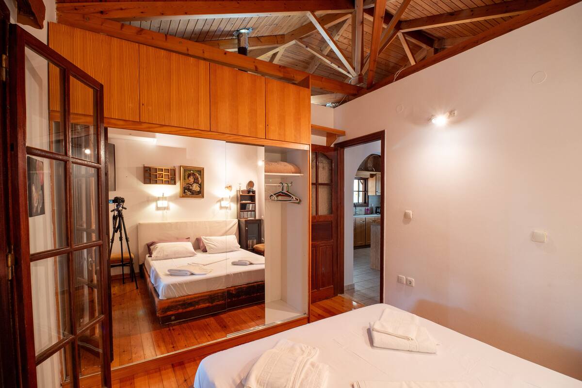 A bedroom with a wooden ceiling, a bed with white linens, a wooden wardrobe, and a mirror reflecting part of the room.