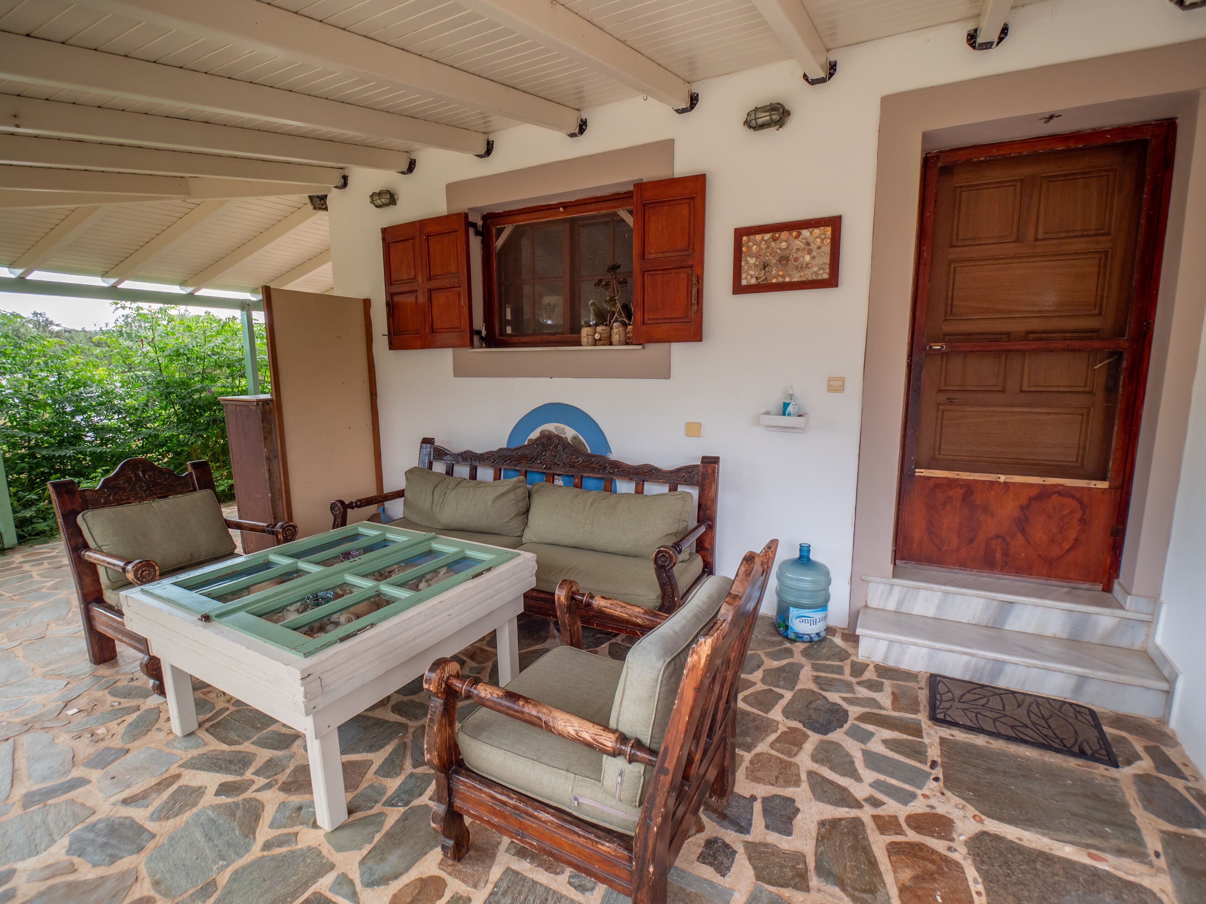 A stone-floored room with a wooden bed, two chairs, a table with a glass top, and a large water dispenser.