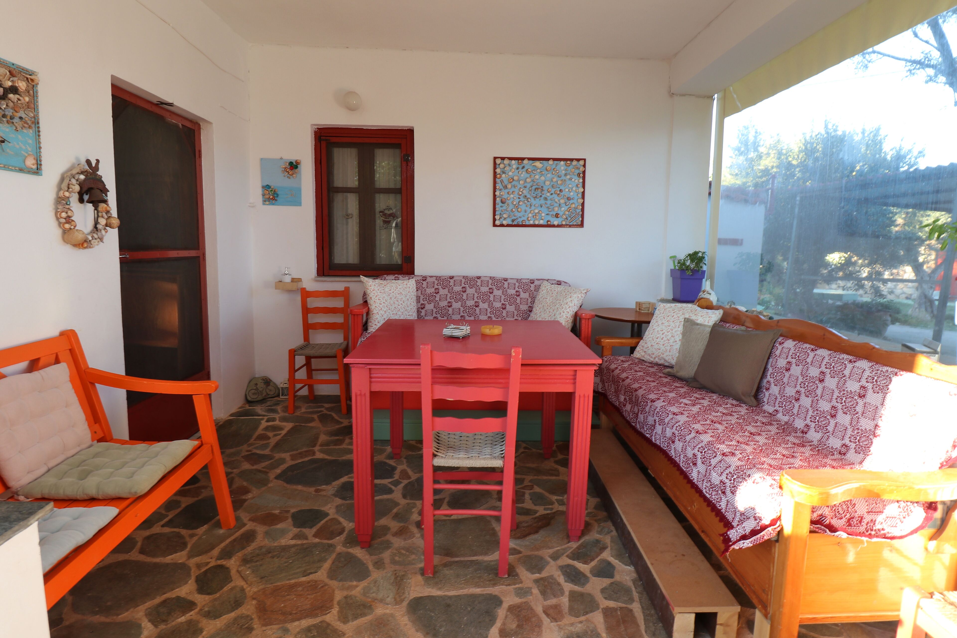 A cozy room with a stone floor, a red table with chairs, a wooden bench, and a patterned sofa.
