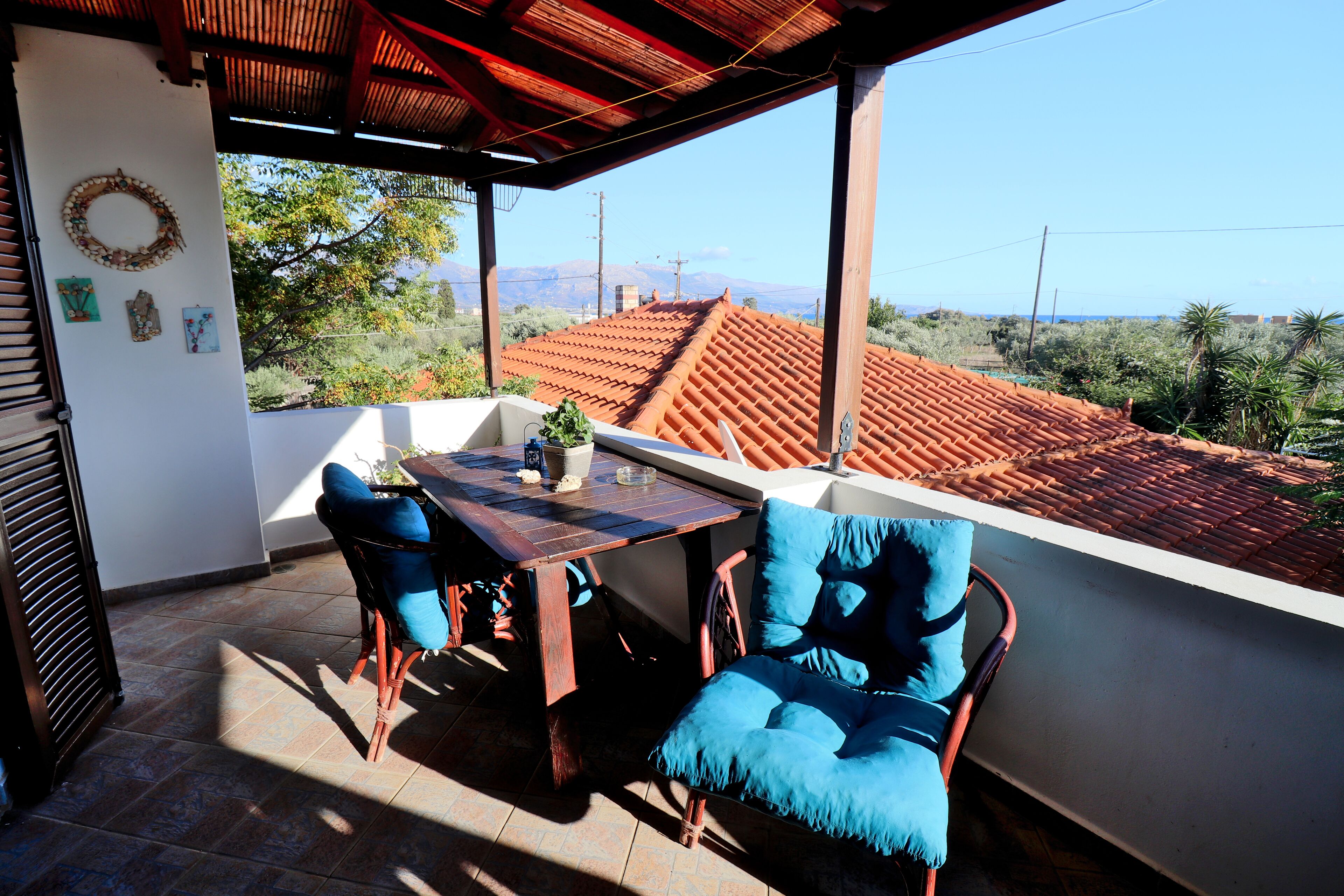 A covered patio with a table and two chairs, overlooking a red-tiled roof and distant mountains.