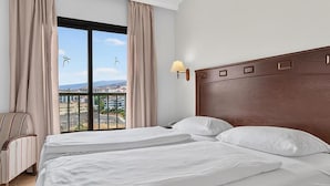 A hotel room with two beds, a view of the city, and a lamp on the wall. - Hapimag Resort Tenerife (Puerto de la Cruz)