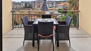 A balcony with a table and chairs, a striped umbrella, and a view of buildings in the distance. - Hapimag Resort Tenerife (Puerto de la Cruz)