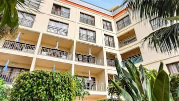 A multi-story hotel with balconies, a courtyard with various plants, and a clear blue sky.