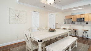A dining area with a white table, four chairs, a bench, and a wall clock.
