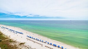 Ein Strand mit blauen Sonnenschirmen und Liegestühlen, ein sandiger Uferstreifen und das Meer.