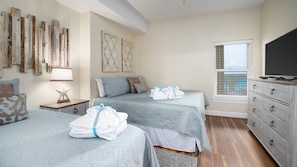 A bedroom with two beds, a dresser, a TV, and artwork on the walls.