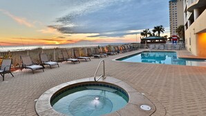 Dachpool-Bereich mit Liegestühlen und Whirlpool, mit Blick auf einen Strand und das Meer bei Sonnenuntergang.