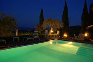 Une piscine au crépuscule, avec des chaises longues et une statue en arrière-plan.