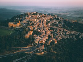 Vista aérea de uma cidade histórica com um castelo imponente, ruas estreitas e uma mistura de edifícios residenciais e comerciais.
