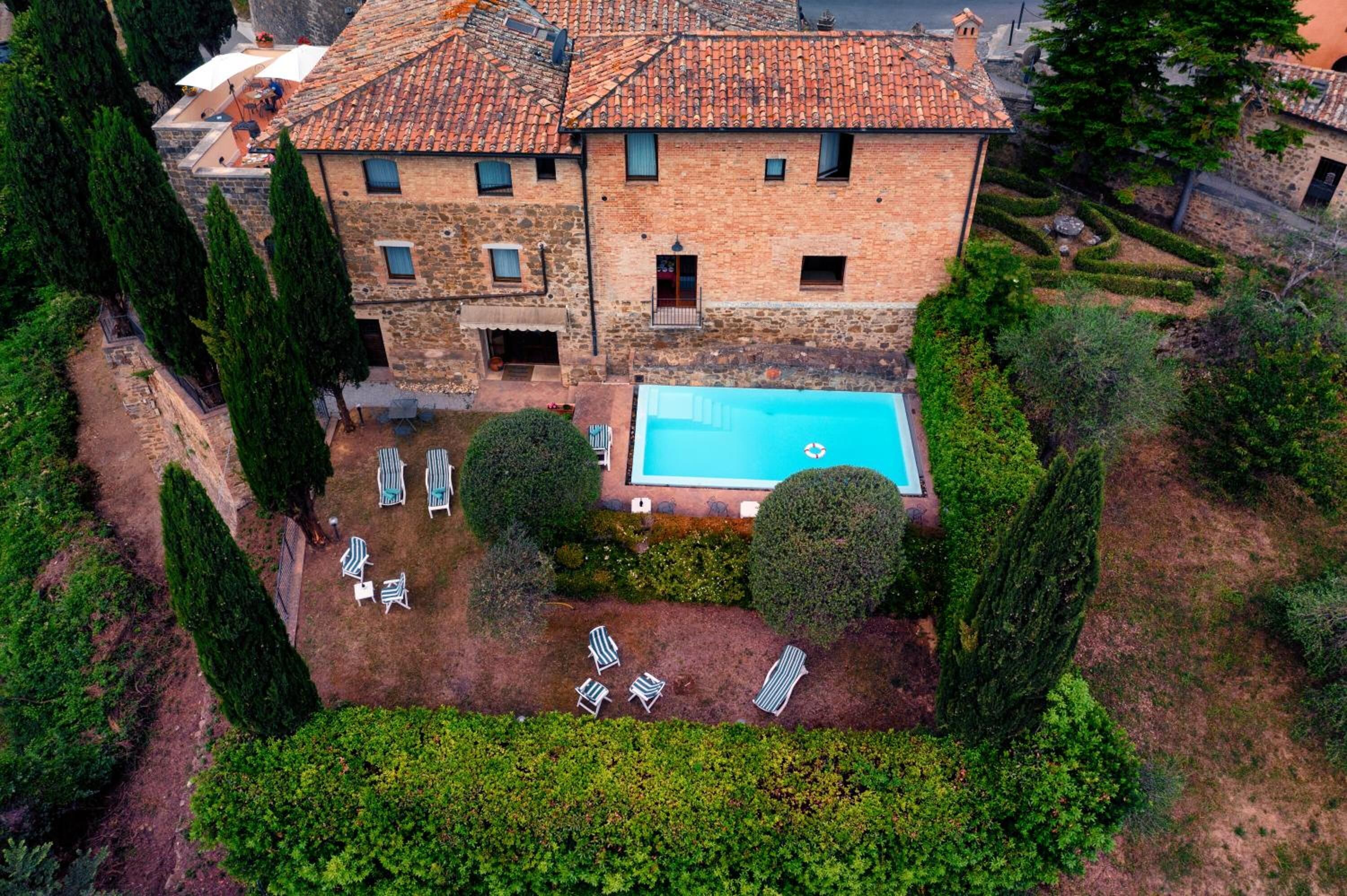 A large stone building with a swimming pool, surrounded by well-maintained gardens and tall trees.