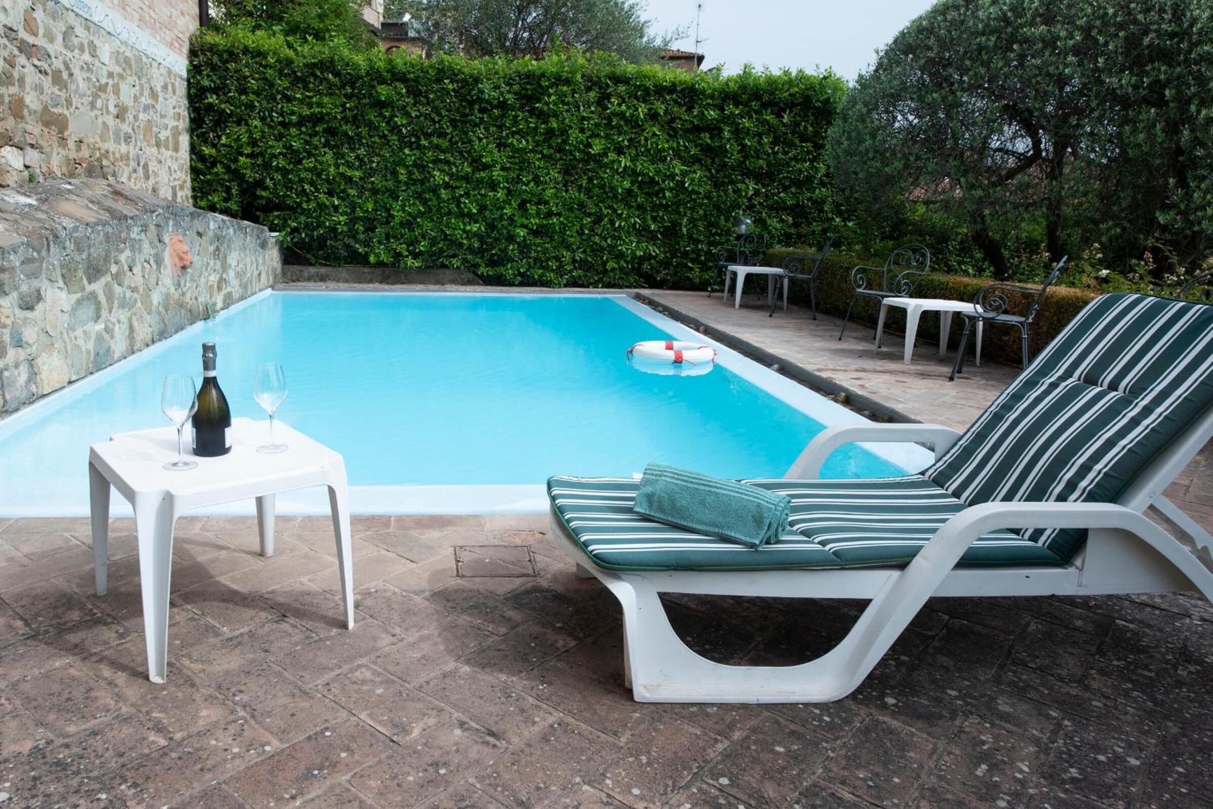 Una piscina con una silla de descanso y una pequeña mesa con una botella y vasos.