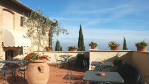 Une terrasse extérieure avec un sol carrelé en terre cuite, des tables et des chaises en métal, des plantes en pot et une vue sur la mer.
