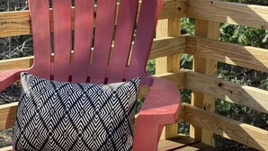 Een rode Adirondack stoel met een gekleurd kussen op een houten terras.