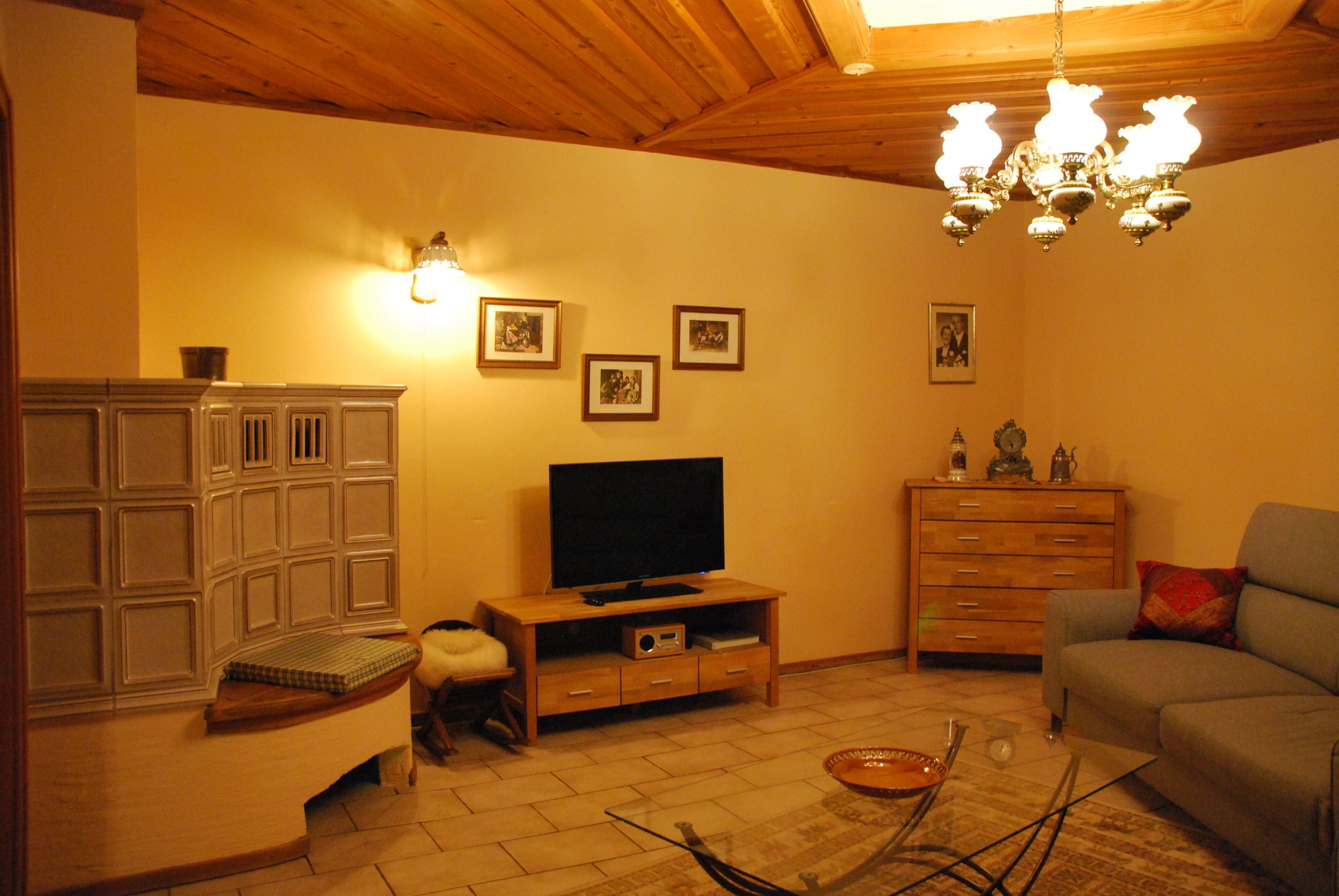 A living room with a television on a wooden stand, a sofa, a cabinet, and a chandelier.