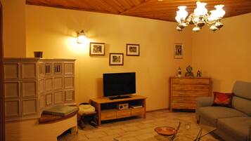 A living room with a television on a wooden stand, a sofa, a cabinet, and a chandelier.