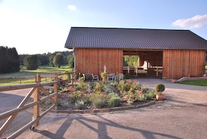A wooden barn with a tiled roof, an open entrance, and a gravel driveway. - Vacation in the Bavarian Forest paradise (Haibach)