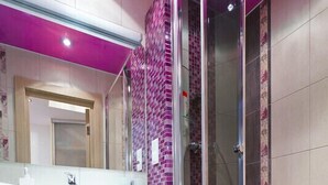 Uma casa de banho moderna com cabine de duche em vidro, toucador branco com gavetas e área de duche com azulejos cor-de-rosa.
