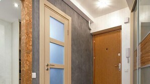 Um corredor com porta de madeira, painéis de vidro jateado, parede com textura de pedra e chão de azulejo.