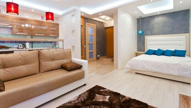 Quarto moderno com uma cama grande, um sofá e uma área de cozinha ao fundo.