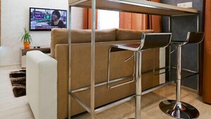 Uma sala de estar moderna com um sofá, dois banquetes, uma mesa de centro com tampo de vidro e uma televisão de tela plana.