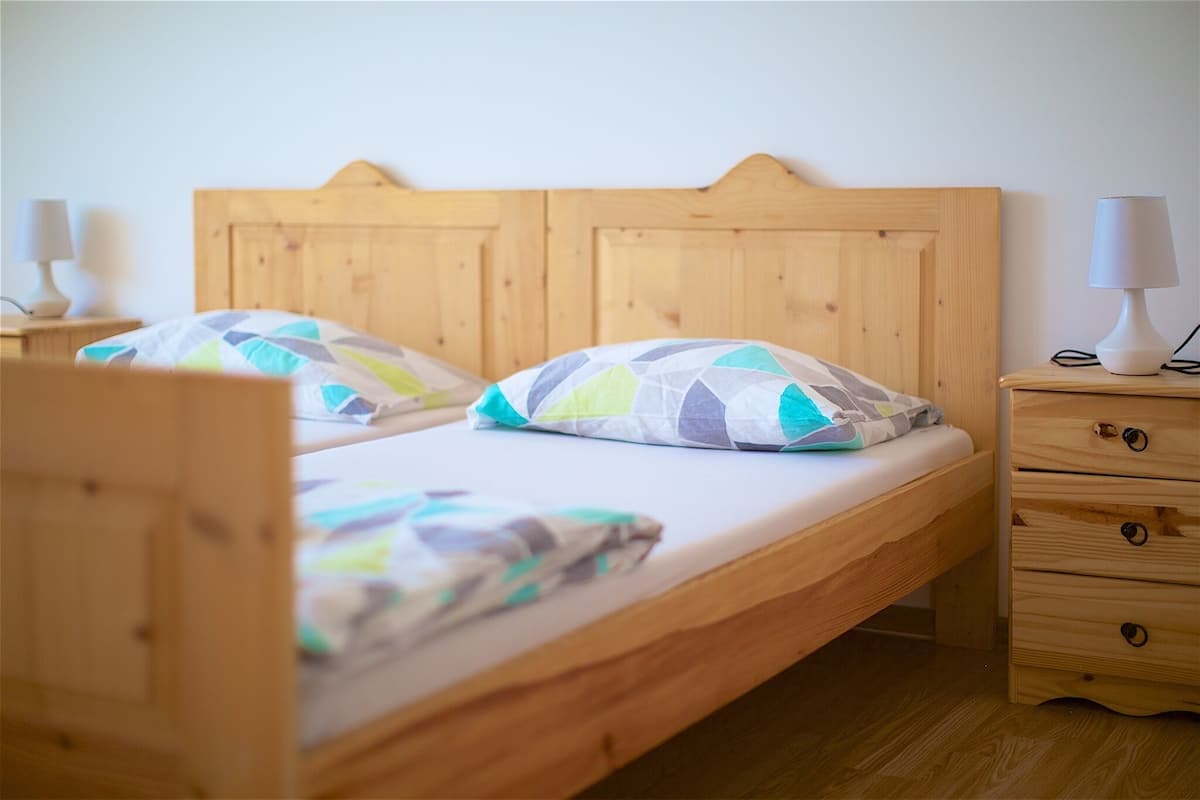A double bed with a wooden headboard, two bedside tables with lamps, and a wooden nightstand with drawers.