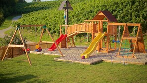 Une aire de jeux en bois, dotée de toboggans et de balançoires, située devant un vignoble.