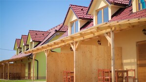 Une rangée de maisons en bois, avec des toits recouverts de tuiles rouges et un patio abrité, aménagé avec du mobilier en bois.