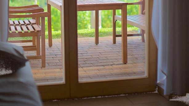 Une porte coulissante à cadre en bois qui donne sur une terrasse extérieure équipée d’une table et de chaises.