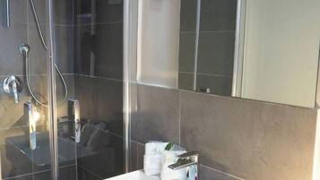 A modern bathroom with a glass shower enclosure, a white sink, and a mirror above it.