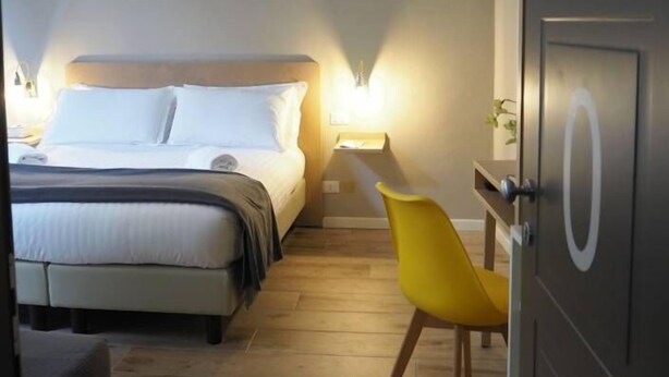 Une chambre d’hôtel avec un lit, une table de chevet, une lampe et une chaise jaune.