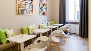 Une pièce avec plusieurs tables et chaises blanches, des coussins verts et des étagères remplies de livres.