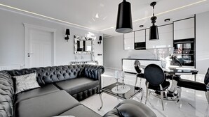 Een moderne woonkamer met een zwarte leren bank, een glazen salontafel, en een eethoek met een zwarte stoel en een kleine tafel.