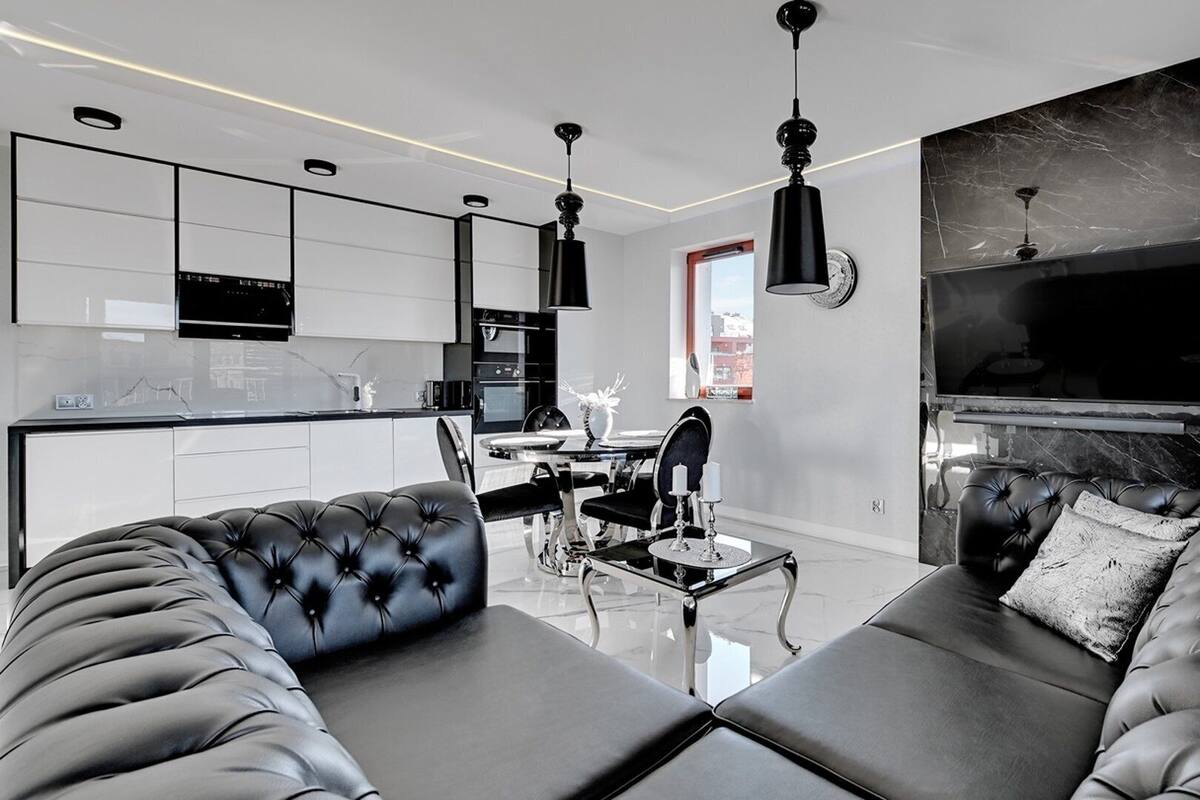 Ein modernes Wohnzimmer mit einer schwarzen Ledersofa, einem Essbereich mit einem Glastisch und einer Küche mit weißen Schränken.