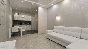 Una sala de estar moderna con un sofá blanco, una zona de comedor con mesa y sillas, y una cocina al fondo.