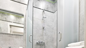 Un baño moderno con ducha envuelta en vidrio, tocador blanco y una pila de toallas blancas.