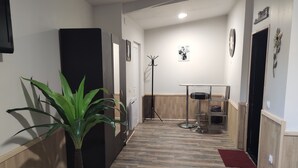 A hallway with a wooden floor, a coat rack, a small table with a chair, and a door with a sign above it. - Guesthouse near Charles De Gaulle Airport (Thieux)