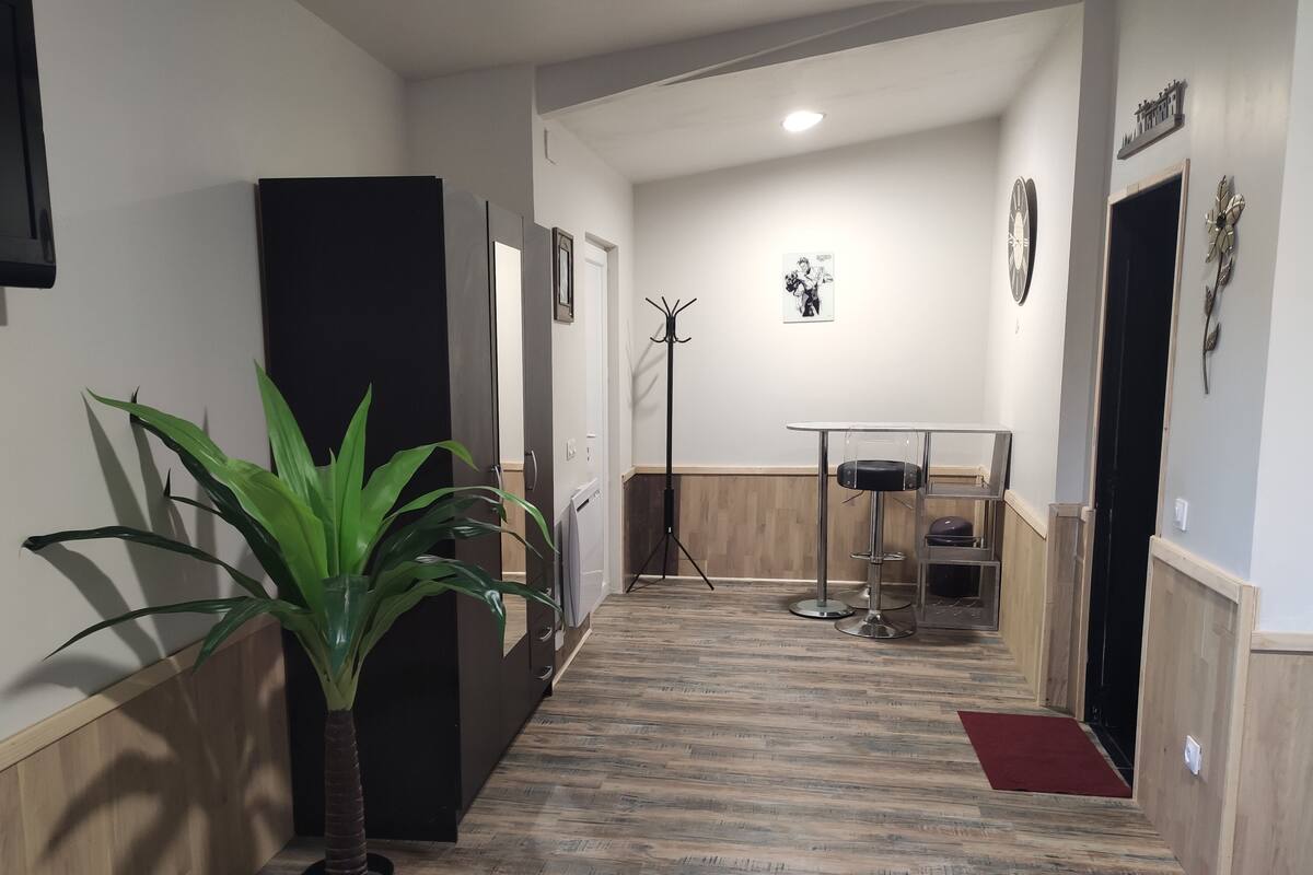Un couloir avec un plancher en bois, un porte-manteau, une petite table avec une chaise et une porte sur laquelle est apposée une pancarte.
