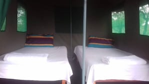 Two twin beds with white linens and colorful pillows, a central pole, and green curtains on the windows. - Paje River Camp (Paje)