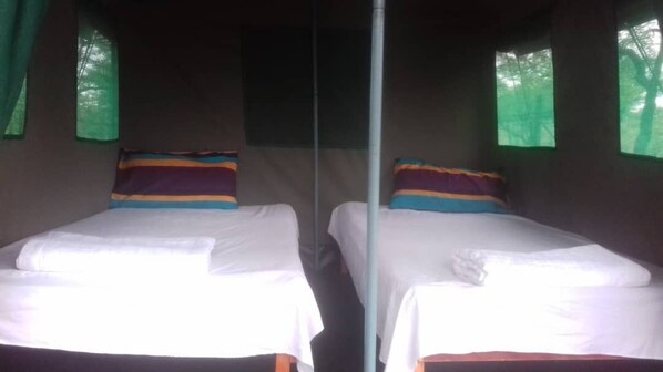 Dos camas individuales con sábanas blancas, almohadas de colores, un poste central y cortinas verdes en las ventanas.